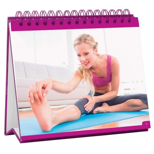 Frau in Trainingskleidung macht Dehnübungen auf einer Yogamatte in einem hellen Wohnzimmer.