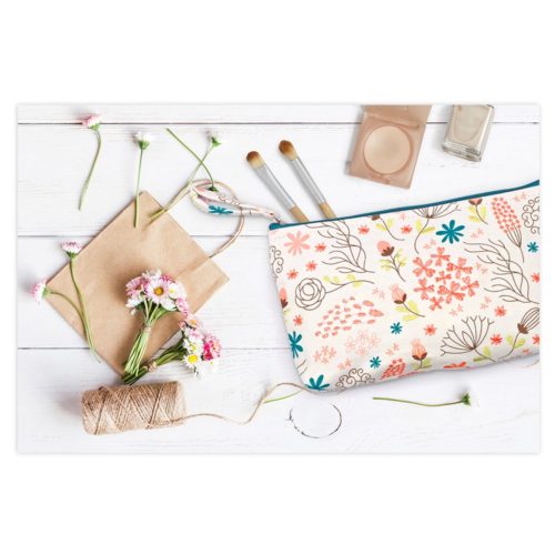 Schminktasche mit Blumenmuster, Pinsel, Blumen, Schnur und brauner Umschlag auf einer weißen Holzoberfläche.