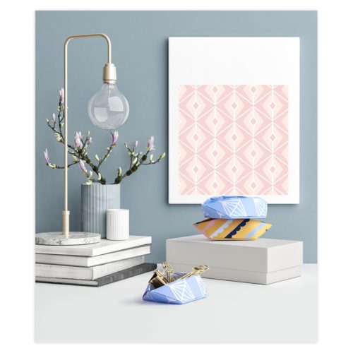 Modernes Deko-Setup mit einer Lampe, Büchern, rosa geometrischer Kunst, einer Vase mit Zweigen und dekorativen Schachteln.