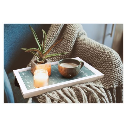 Gemütliches Ambiente mit einer Decke, einer Kerze, einer Pflanze und einer Tasse Kaffee auf einem Tablett.