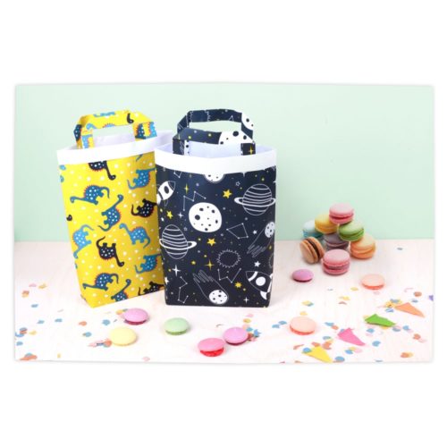 Zwei bunte Geschenktüten mit Dinosaurier- und Weltraummotiven, umgeben von verstreuten Macarons und Konfetti.