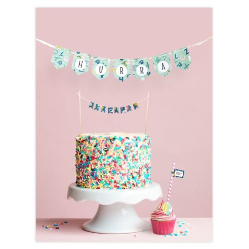 Bunter Streuselkuchen und Cupcake auf einem Ständer mit „HURRA“-Banner vor rosa Hintergrund.