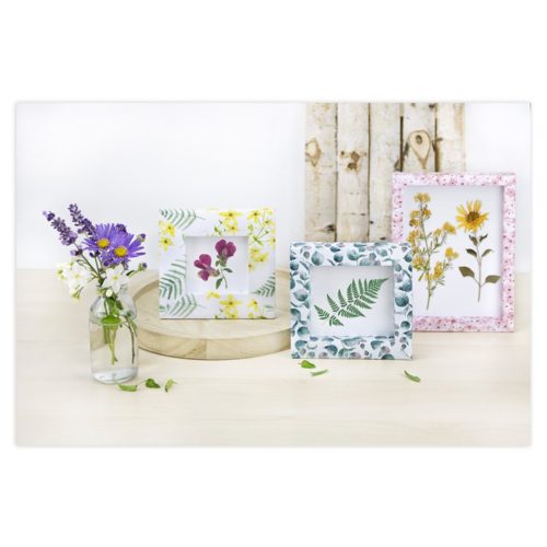 Bilderrahmen mit Blumenmotiven und eine Vase mit Wildblumen auf einer hellen Holzoberfläche.