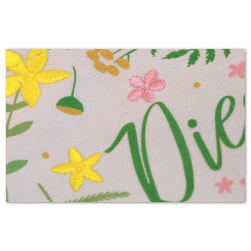 Blumenstickerei mit „Die“ in grünem Text auf weißem Stoffhintergrund.