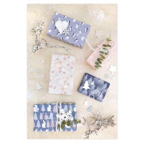 Dekorative Geschenkboxen mit weihnachtlichem Geschenkpapier, umgeben von Schneeflocken und getrockneten Zweigen.
