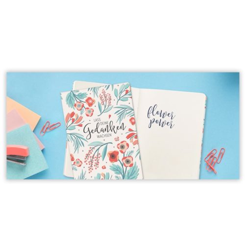 Zwei Notizbücher mit Blumenmuster auf blauem Untergrund mit Büroklammern, Haftnotizen und einem Hefter.