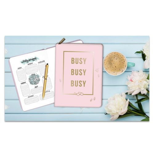 Planer, Notizbuch mit „Busy Busy Busy“-Umschlag, Stift, Kaffeetasse und weiße Blumen auf einem blauen Holztisch.