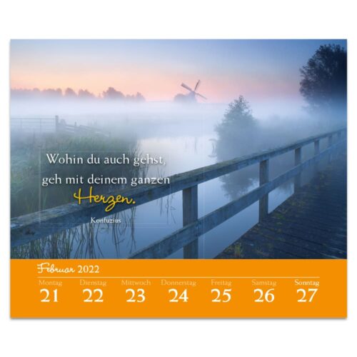 Eine neblige Landschaft mit einer Windmühle, einer Brücke und einem inspirierenden deutschen Text auf einem Kalender für Februar 2022.