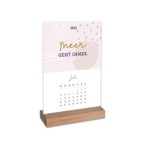 Dekorativer Tischkalender 2022 auf Holzständer mit Anzeige für Juli, abstraktem Hintergrund und „Meer geht immer“.