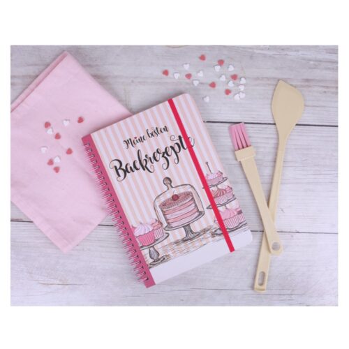 Rezeptbuch mit Kuchenillustrationen, rosa Tuch, Herzstreuseln, Spatel und Pinsel auf Holztisch.