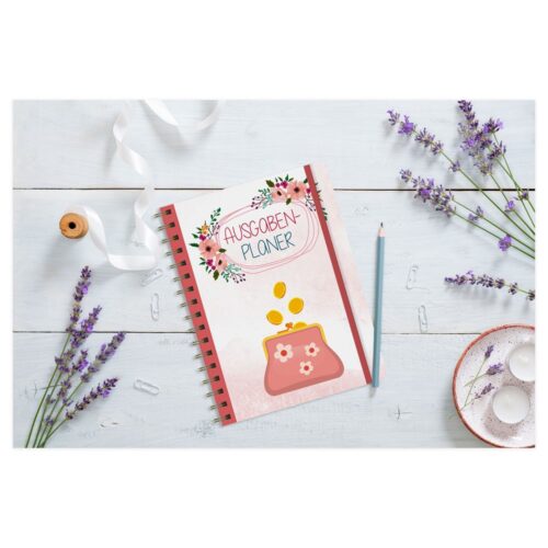 Ein Ausgabenplaner-Notizbuch auf einem weißen Holztisch mit Lavendel, einer Schleife, einem Bleistift und kleinen Tellern.