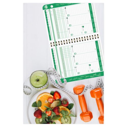 Fitnessplaner mit Früchten, Maßband, Hanteln und einem offenen Tagebuch auf einer weißen Fläche.
