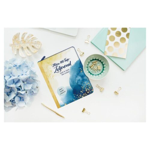 Ein Tagebuch, blaue Blumen, goldene Clips und dekorative Artikel auf einer weißen Oberfläche.