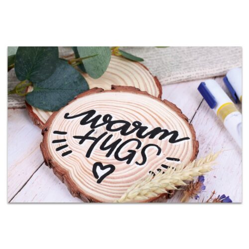 Holzscheibe mit der Aufschrift „Herzliche Umarmungen“, umgeben von Grün, Weizen und Markierungen.