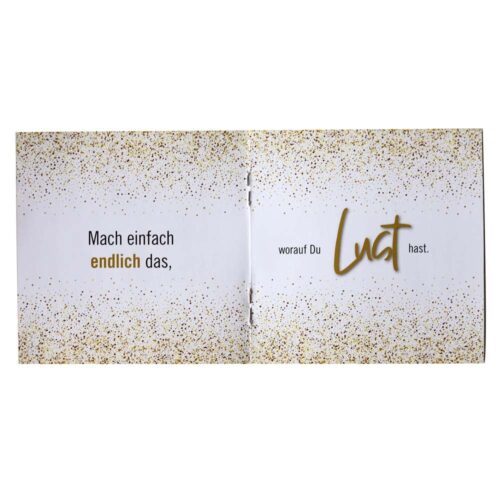 Offenes Buch mit deutschem Text und Goldglitzer-Design auf weißen Seiten.