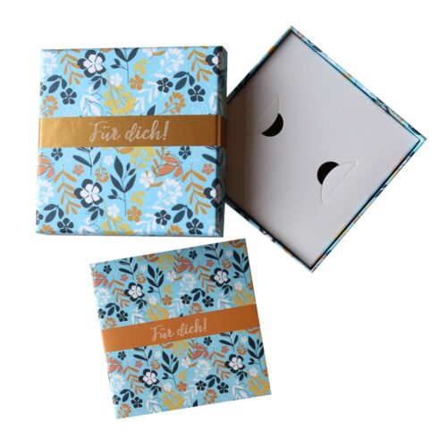 Blaue Geschenkbox mit Blumenmuster und dem Text „Für dich!“, teilweise geöffnet, mit schlichtem Innenleben.