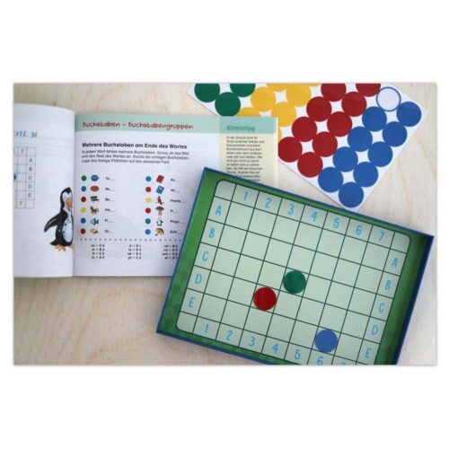 Aufgeschlagenes Rätselbuch mit Pinguin, Gitterbrettspiel mit roten und grünen Teilen und Blatt mit farbigen Punkten auf einem Tisch.