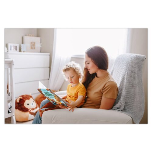 Frau liest einem Kind in einem gemütlichen Zimmer ein Buch vor, durch das sanftes Sonnenlicht fällt.