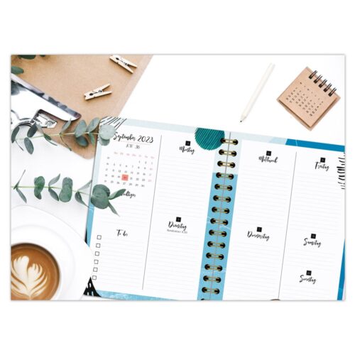 Aufgeschlagener Planer für September 2023, Kaffeetasse und Eukalyptus auf einem Schreibtisch mit einem kleinen Kalender.