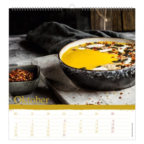 Eine Kalenderseite für Oktober mit einer Schüssel cremiger Suppe, garniert mit Körnern und Gewürzen.