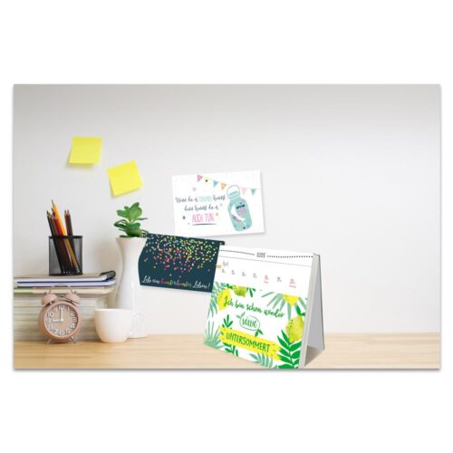Schreibtisch mit Kalender, gestapelten Büchern, einer Pflanze, einer Tasse und Haftnotizen an einer Wand.